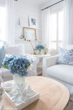 a living room with white furniture and blue flowers in the vase on the coffee table