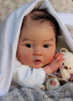 a baby is holding a teddy bear under a blanket