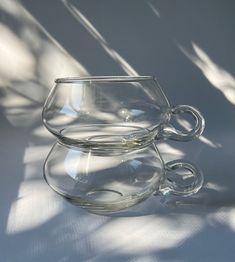 two clear cups sitting on top of each other in front of a white wall with shadows