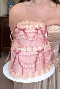 a woman holding a three tiered cake with pink icing and bows on it