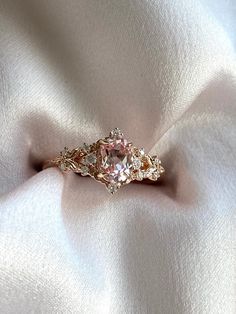 a pink diamond ring sitting on top of a white cloth