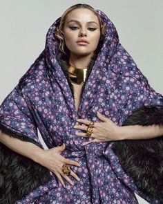 a woman wearing a purple and black robe with fur stoler on her head, in front of a white background