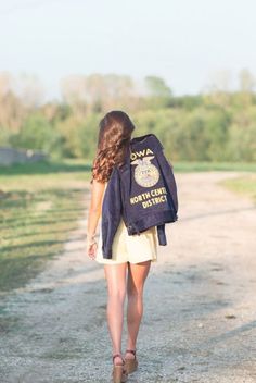 a woman walking down a dirt road with a jacket on her back