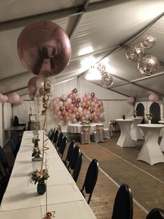 a party tent with tables and balloons on the ceiling, white tablecloths and black chairs