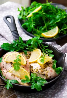 two pans filled with chicken, lemon and parsley on top of a table