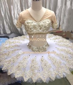 a mannequin wearing a white and gold dress with flowers on the skirt, sitting on a table