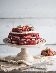 a cake with strawberries and blueberries is on a plate next to some berries