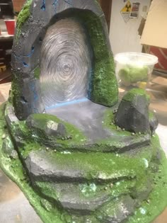 there is a sculpture made out of rocks and green moss on the counter top in front of it