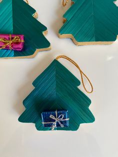 three wooden christmas trees with presents tied to them on a white surface, one is green and the other is blue