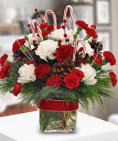 a vase filled with red and white carnations, candy canes and pine cones