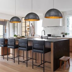 a kitchen island with four stools in front of it and three pendant lights hanging from the ceiling