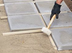 a man is laying tile on the ground with a hammer in his hand and he's working on it