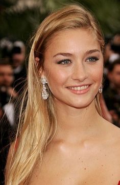 a woman with long blonde hair and blue eyes smiles at the camera while standing in front of photographers