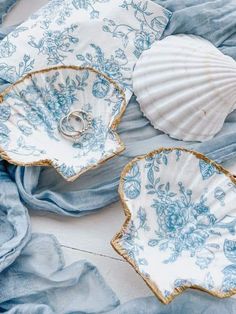 two wedding rings are placed in the center of blue and white dishes with seashells on them