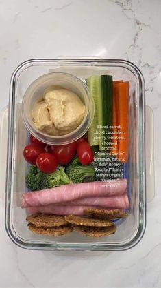 a plastic container filled with meat, vegetables and hummus on top of a table