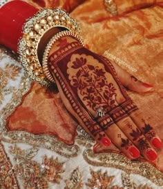 a woman's hand painted with henna and jewelry on top of a bed