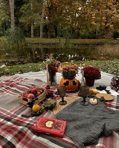 a picnic table with pumpkins, flowers and other items on it in front of a pond