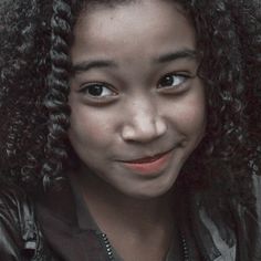 a close up of a person wearing a jacket and smiling at the camera with curly hair