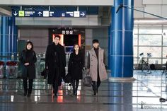 four people standing in an airport waiting for their luggage