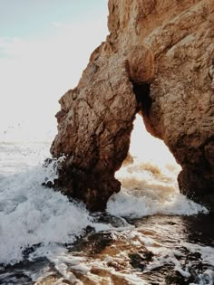 a rock formation with water coming out of it and the sun shining through its opening