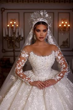 a woman wearing a wedding dress with long sleeves and a veil on her head is standing in front of a chandelier