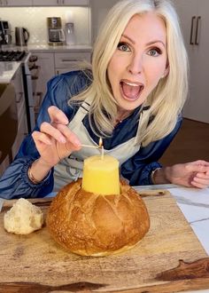 a woman holding a lit candle in front of a loaf of bread on a cutting board