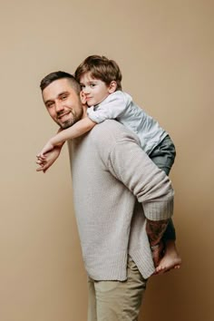 a man holding a little boy on his shoulders in front of a brown background,