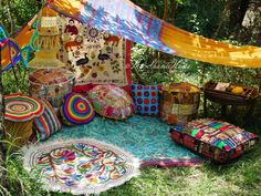 an outdoor area with several colorful pillows and rugs on the ground in front of trees