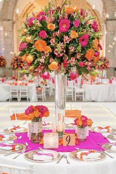 a tall vase filled with lots of colorful flowers on top of a white table cloth