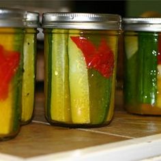 four jars filled with pickles sitting on top of a counter