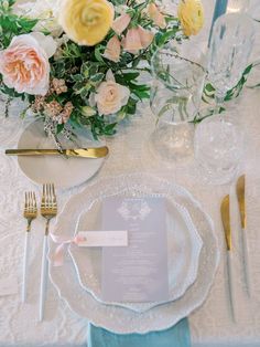 the table is set with white and gold place settings, silverware, and floral centerpieces