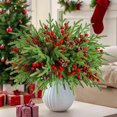 a white vase filled with red berries and pine cones on top of a wooden table