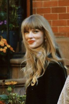 a woman with long blonde hair and bangs walking down the street in front of a brick building