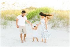 an adult and two children holding hands while walking on the beach with grass in the background