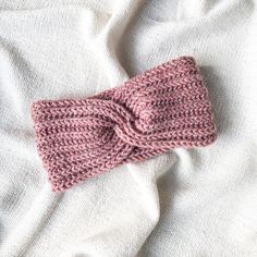 a pink knitted headband laying on top of a white bed sheet with a knot in the middle