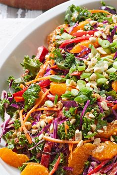 a salad with oranges, broccoli and nuts in a white bowl