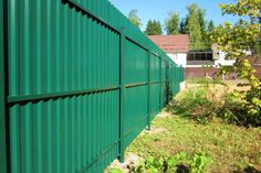 a green metal fence in the middle of a grassy area with trees and buildings behind it