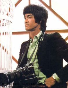 a man holding a camera in his right hand while wearing a suit and green shirt