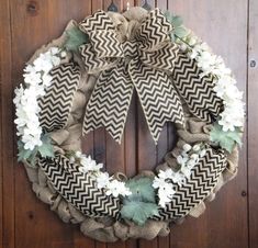 a burlock wreath with white flowers and greenery hangs on a wooden door