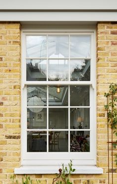 an open window on the side of a brick building with potted plants in front