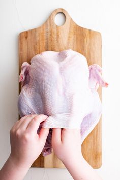 a person holding a piece of raw chicken on a cutting board