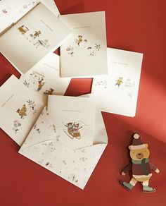 several cards and a toy bear on a red surface with white envelopes in the shape of santa's sleigh