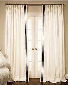 two white vases sitting next to each other in front of a window with curtains