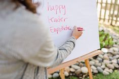 a woman writing on a happy teacher's board in front of some rocks and grass