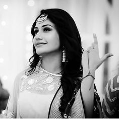 a woman with long hair and jewelry making the v sign while standing in front of other people