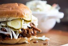 a pulled pork sandwich with coleslaw and pickles on a wooden cutting board