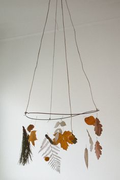 a mobile with leaves hanging from it's sides in a white walled room next to a window