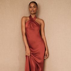 a woman standing in front of a wall wearing a red dress with a halter neck