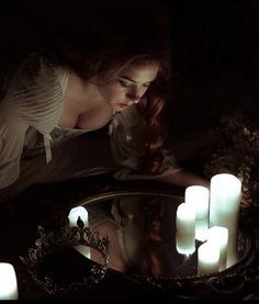 a woman is looking at candles in front of a mirror on the floor with her head down