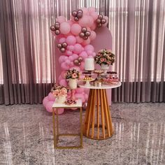 a table topped with cakes and desserts next to a pink wall covered in balloons